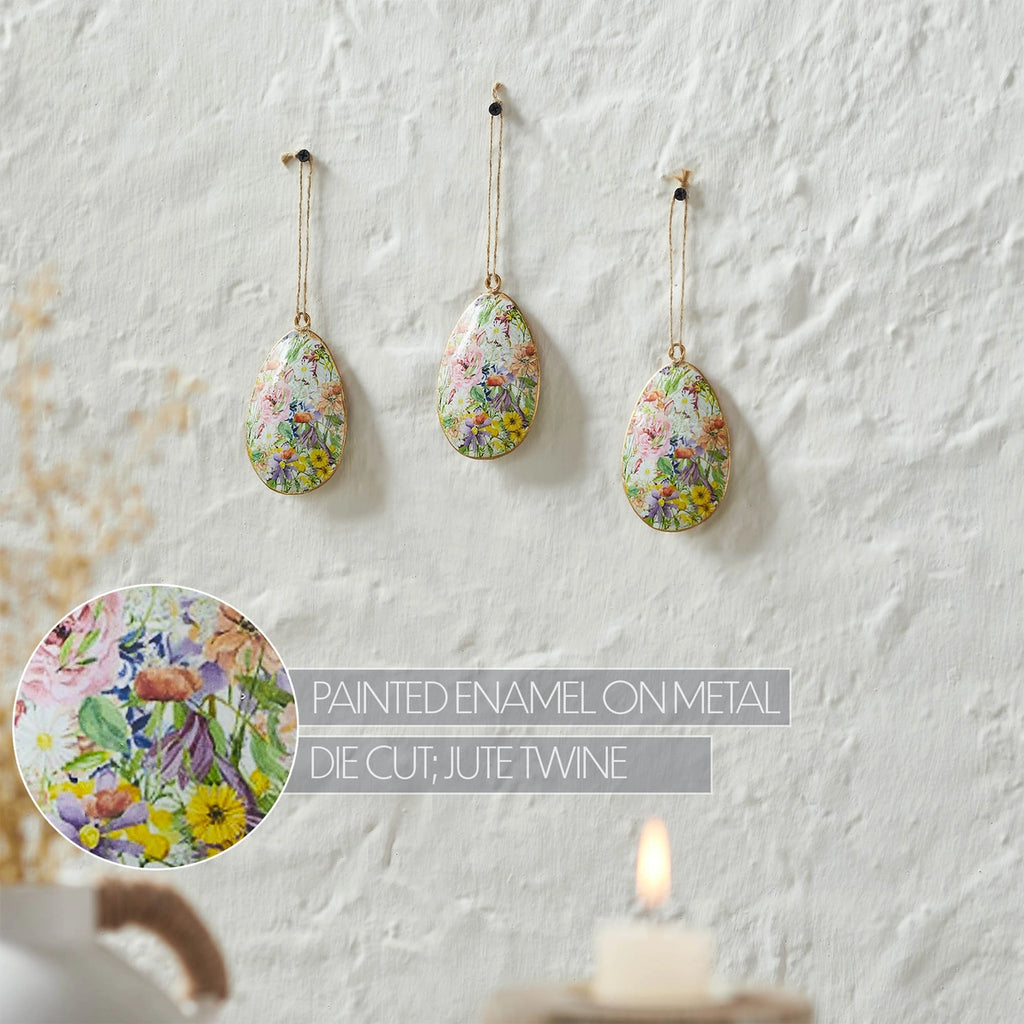 Three floral teardrop ornaments hanging on a textured white wall with an inset showing the painted design.