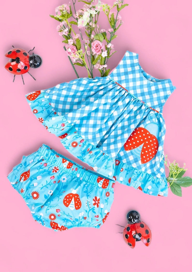 Children's blue checkered outfit with floral patterns on a pink background with ladybug decorations.