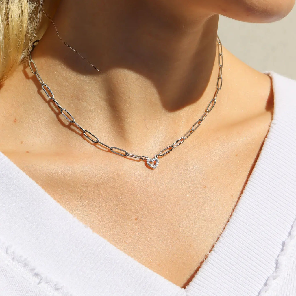 Silver chain necklace with a small pendant on a person wearing a white sweater.