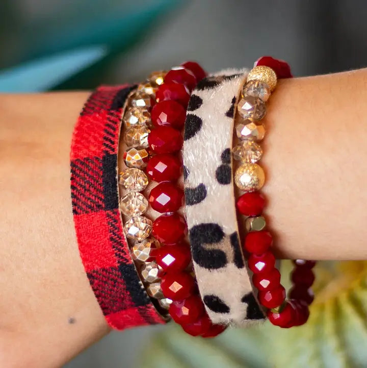 Close-up of a wrist wearing multiple bracelets with red and gold beads, plaid pattern, and leopard print.