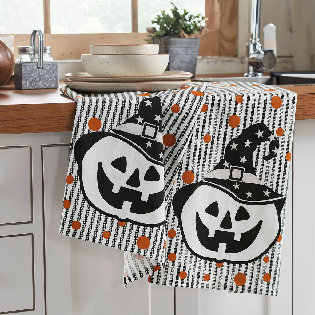Halloween-themed dish towel with pumpkins and witch hats on a kitchen counter.