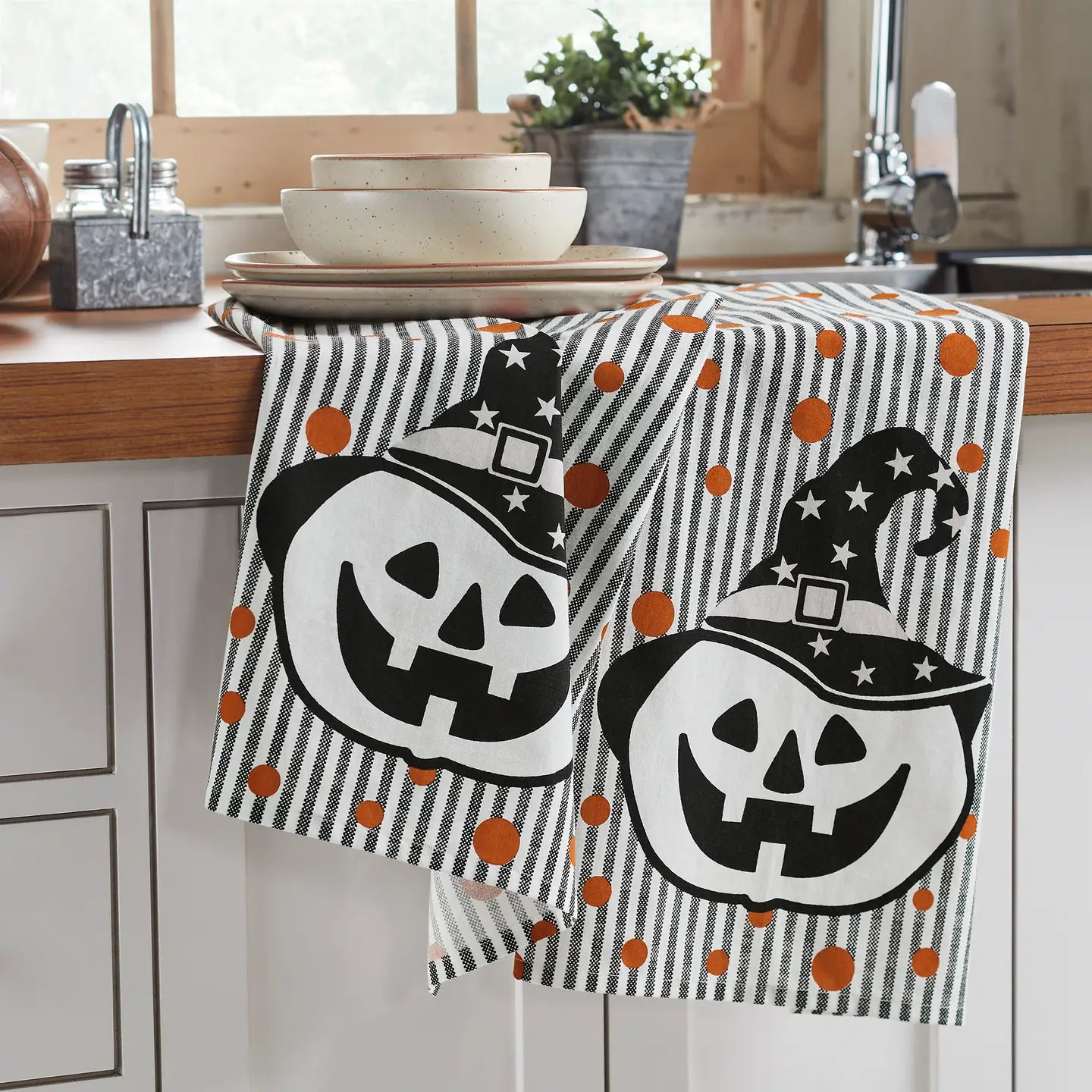 Halloween-themed dish towel with pumpkins and witch hats on a kitchen counter.