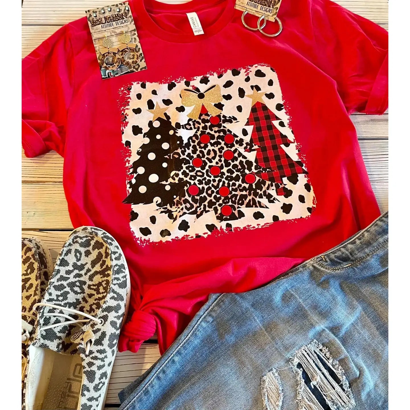Red t-shirt with patterned design, leopard print shoes, and jeans on a wooden surface