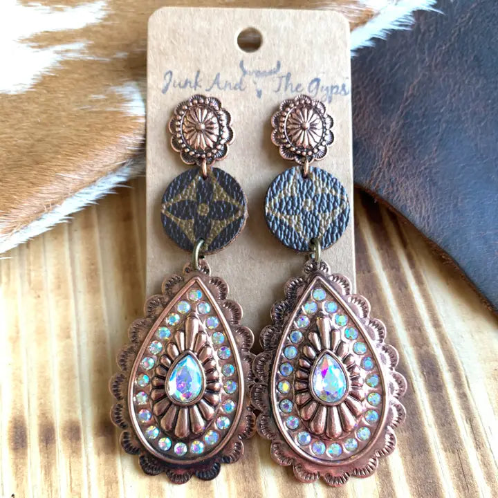 Pair of ornate earrings on a wooden surface with 'Junk and the Gyps' branding.