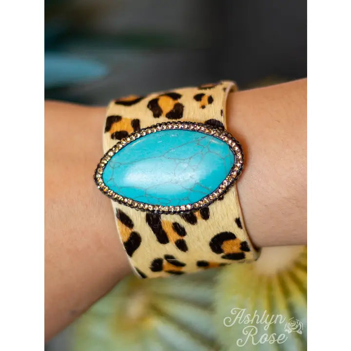 Leopard print cuff bracelet with a turquoise stone on a wrist, brand 'Ashlyn Rose' visible.