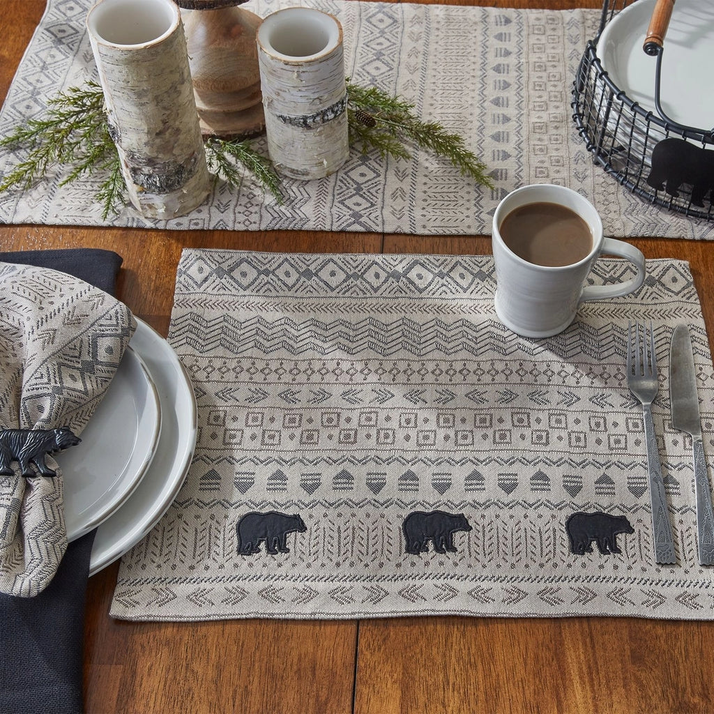 Table setting with a patterned placemat featuring bears, a mug of coffee, and cutlery on a wooden table.