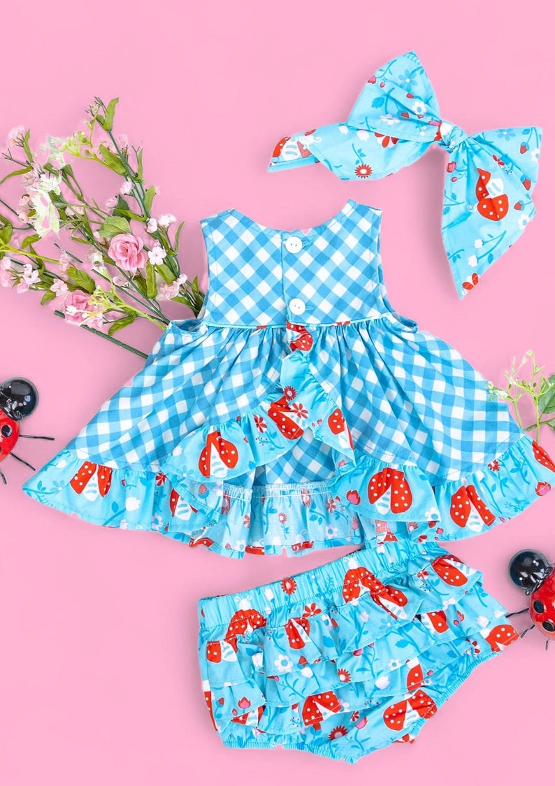 Children's blue checkered dress with red ladybug pattern on a pink background