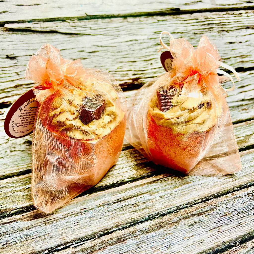 Two wrapped bath bombs on a wooden surface with a sheer orange ribbon.