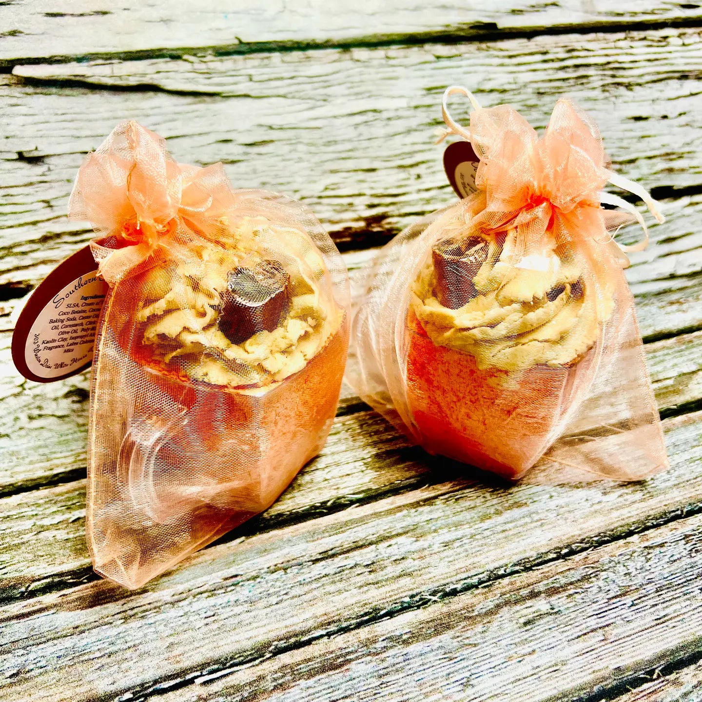 Two wrapped bath bombs on a wooden surface with a sheer orange ribbon.
