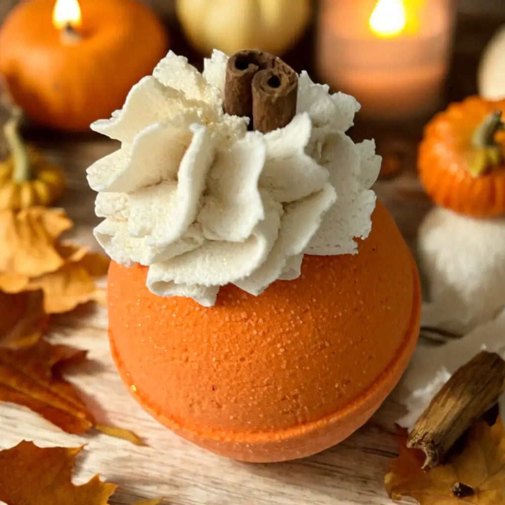Orange bath bomb with whipped cream and cinnamon stick on a wooden surface with pumpkins and candles in the background