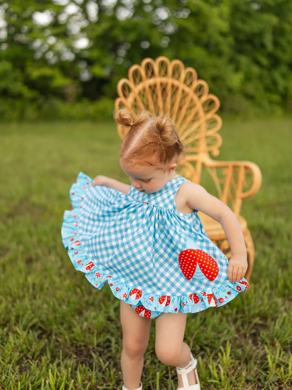 Child wearing a blue checkered dress with red strawberry pattern outdoors.