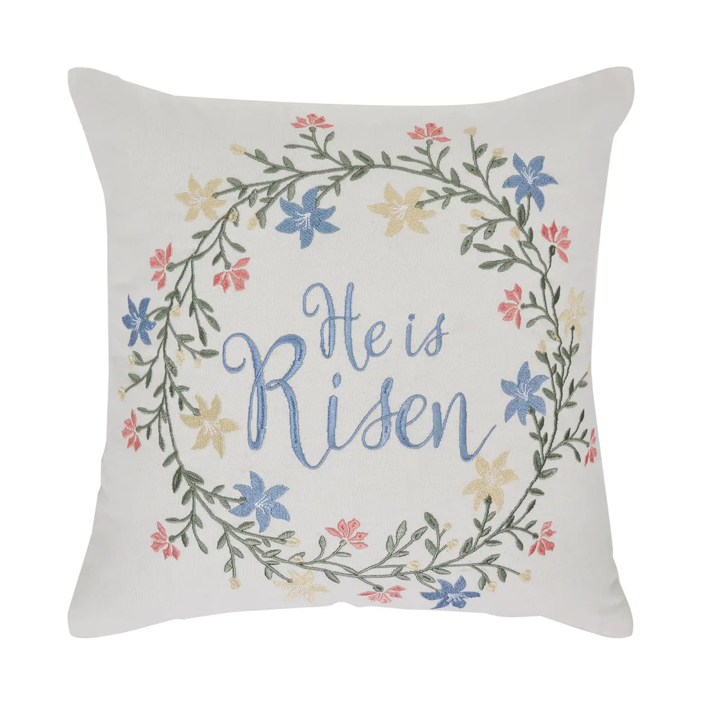 Decorative pillow with floral wreath and 'He is Risen' text on a white background