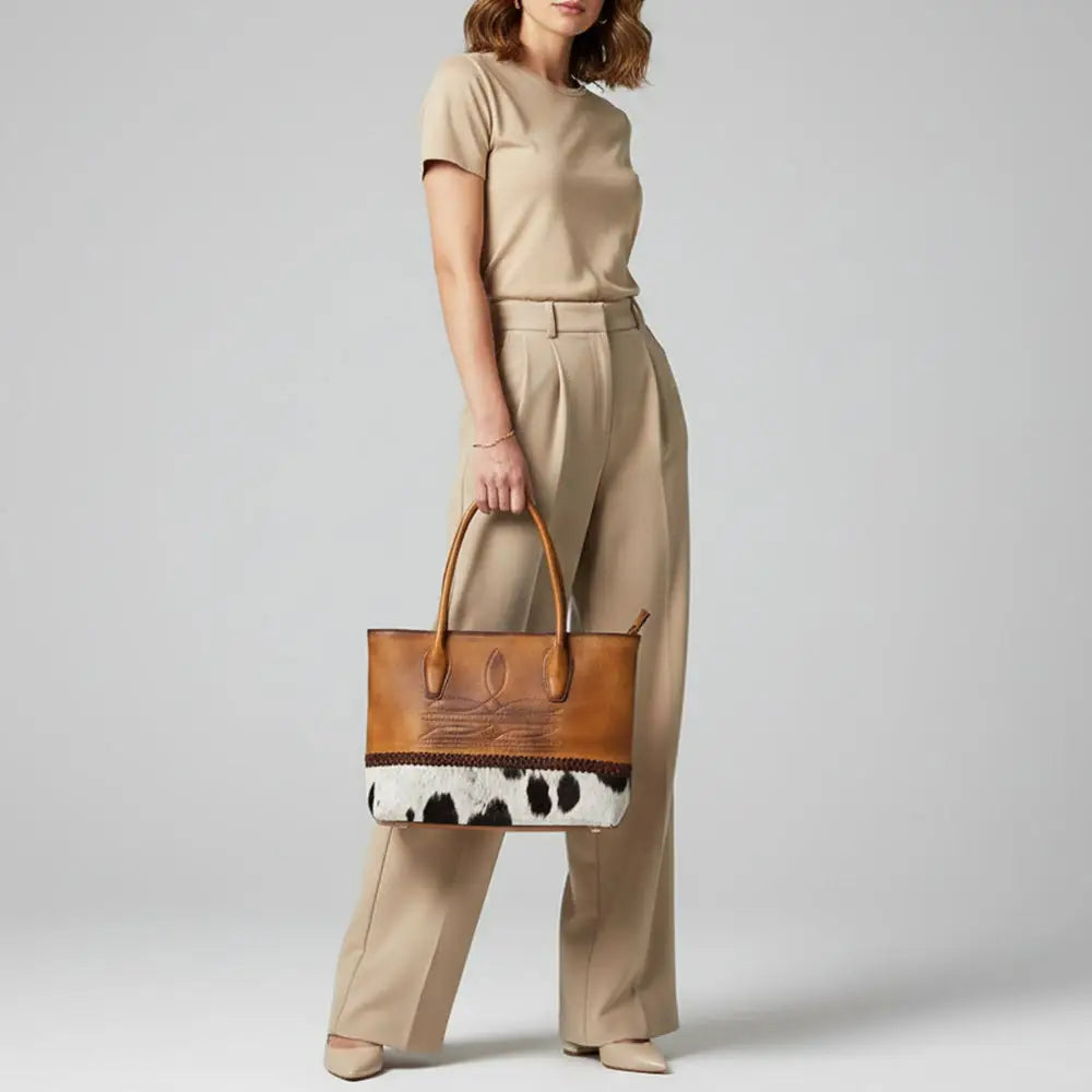 Woman holding a brown leather handbag with cowhide pattern against a plain background