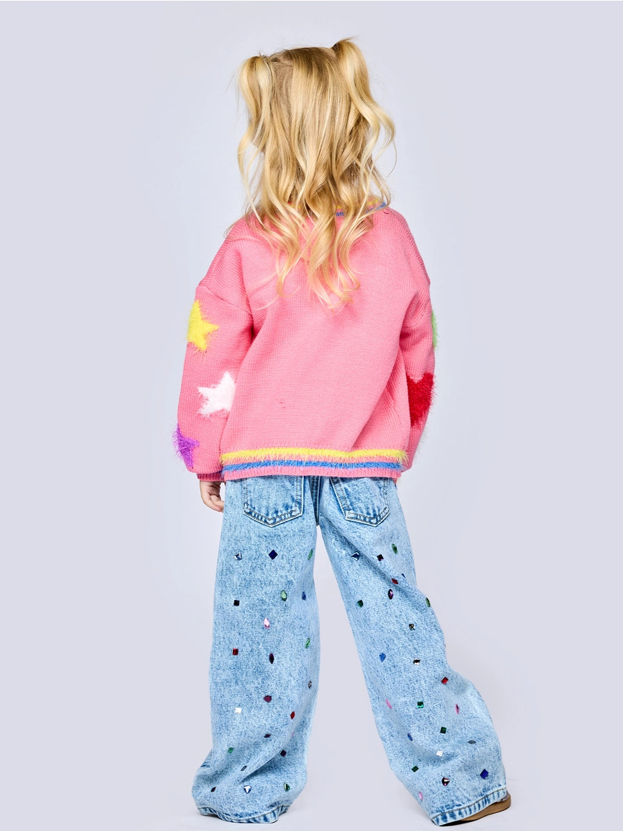 Child wearing a pink sweatshirt with colorful accents and light blue jeans with star patterns on a plain background