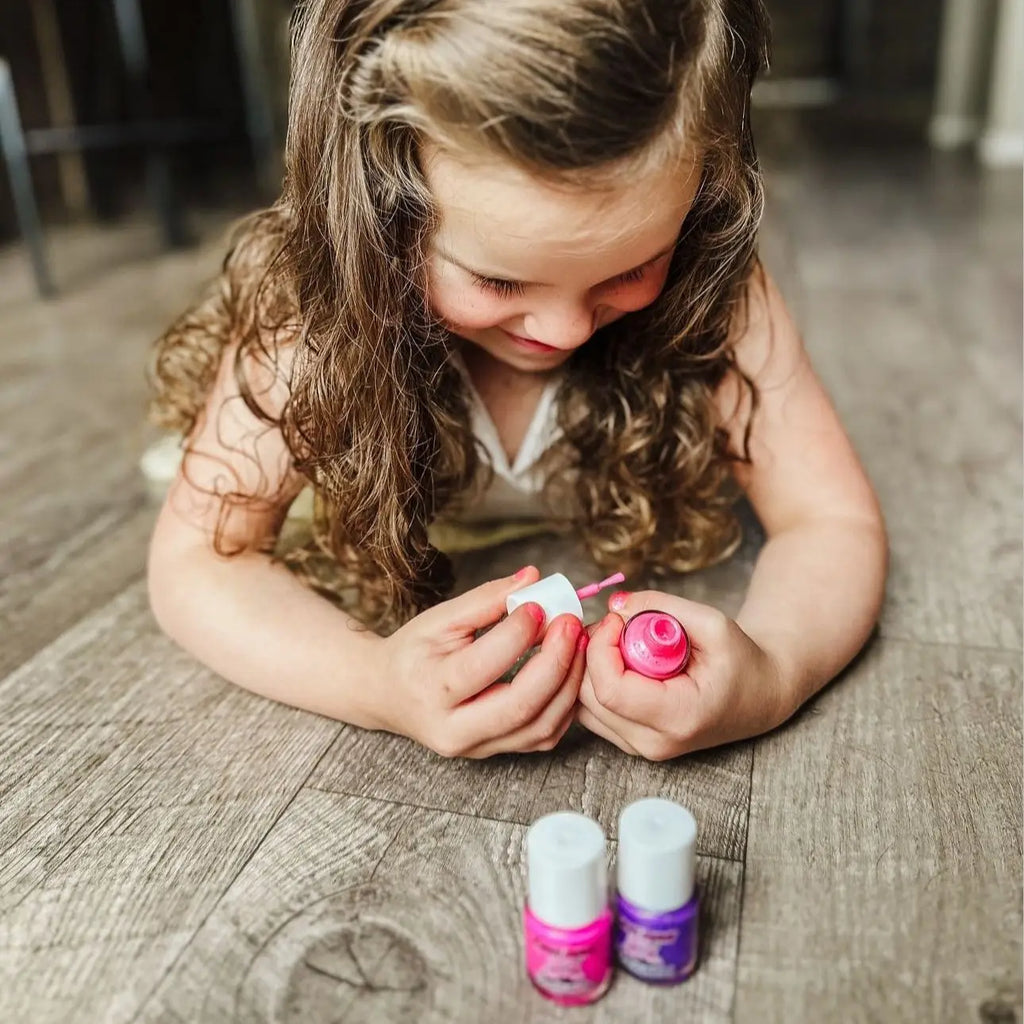 Young girl playing with nail polish bottles on a wooden floor