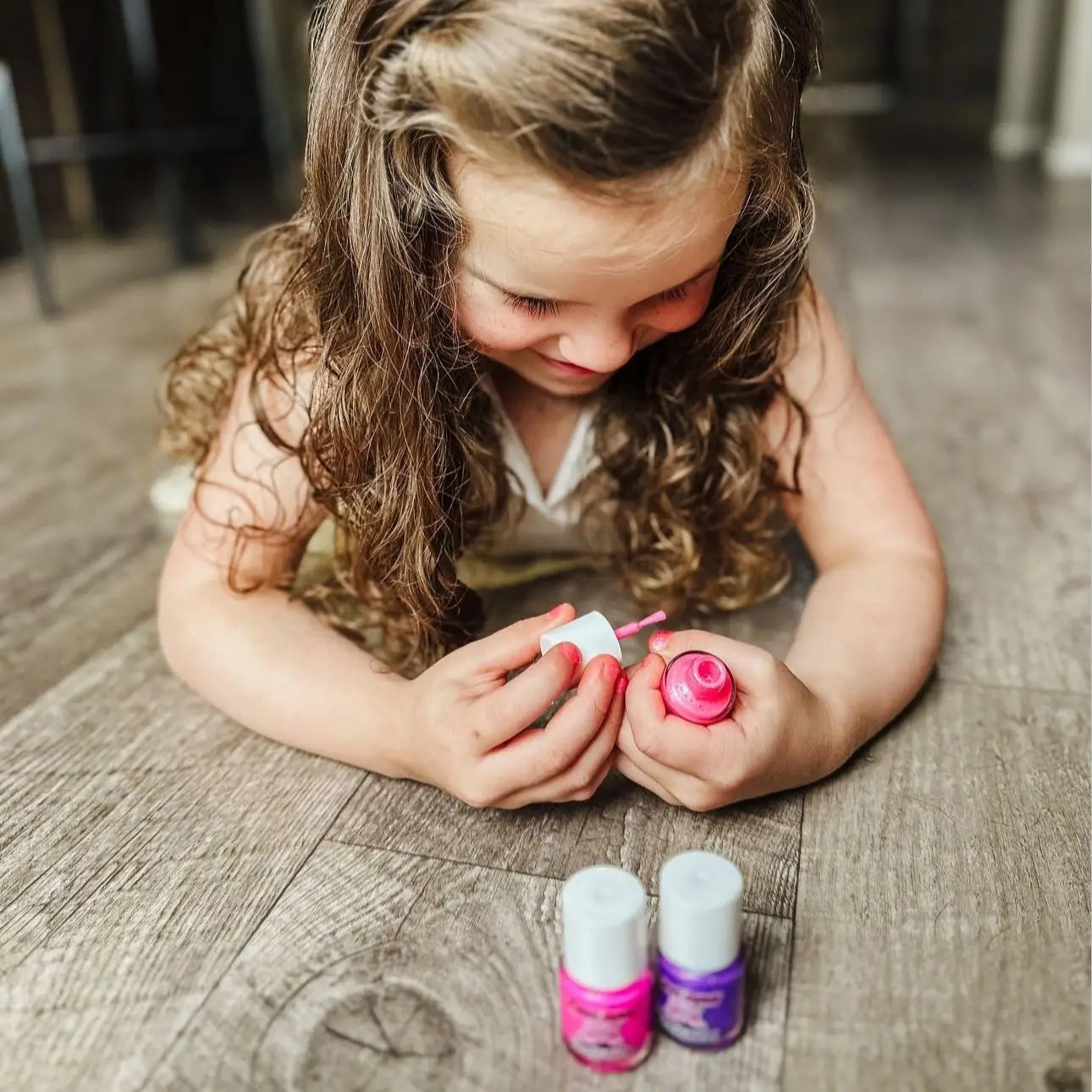 Young girl playing with nail polish bottles on a wooden floor