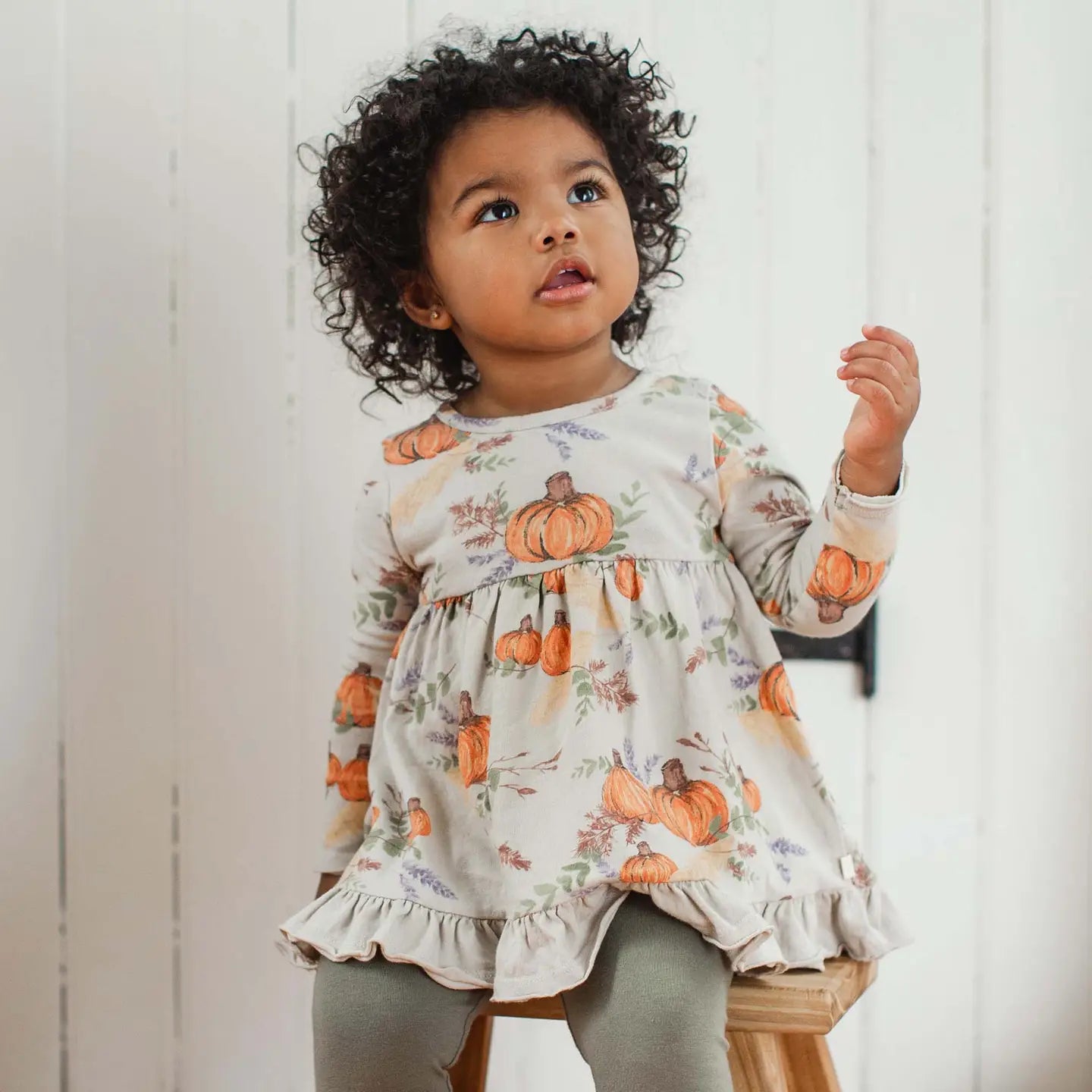 Child wearing a dress with pumpkin prints against a white background