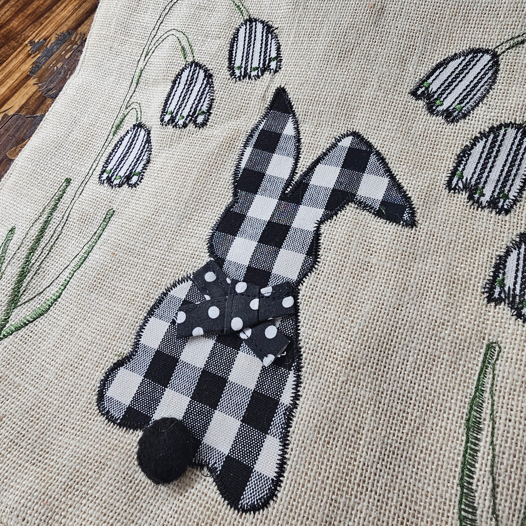 Black and white checkered bunny toy on a textured fabric background with floral embroidery