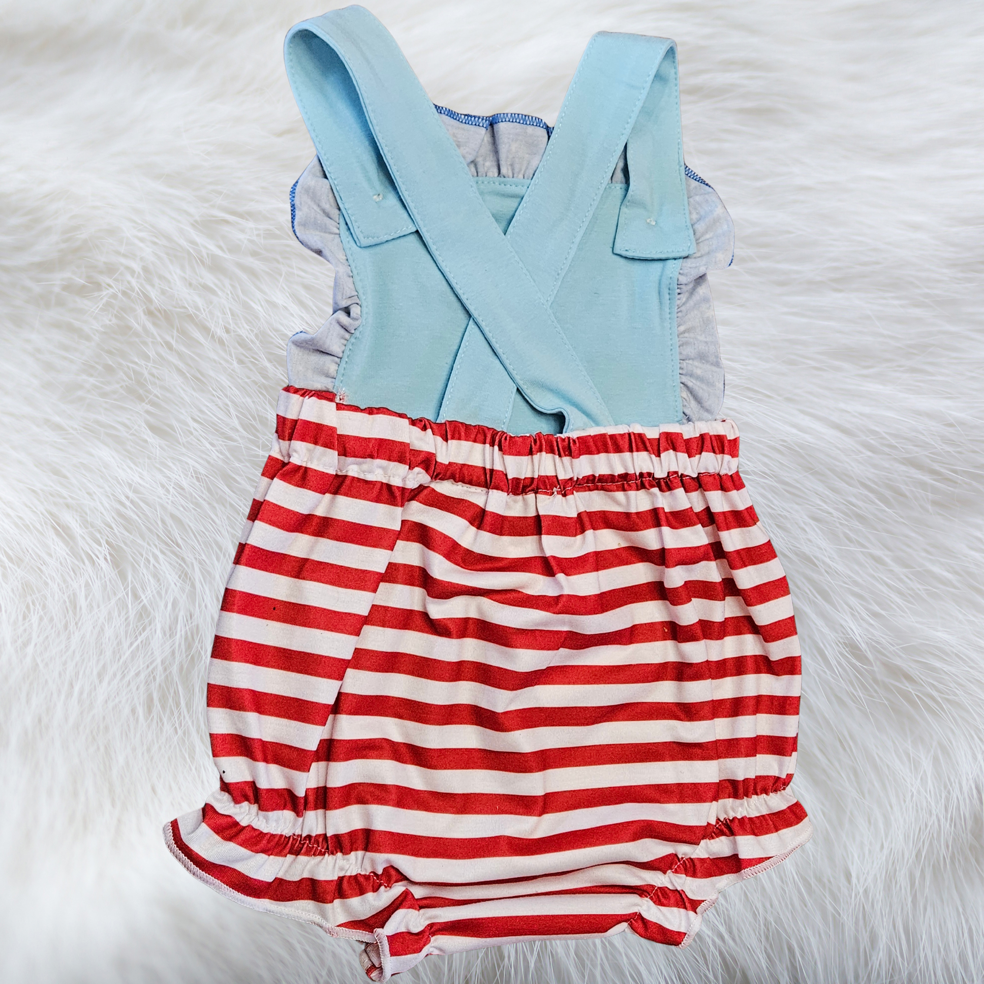 Baby romper with light blue top and red and white striped skirt on a fluffy white surface
