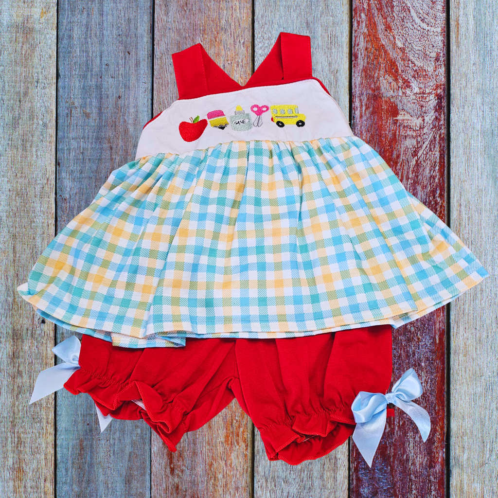 Children's outfit with checkered dress and red bloomers on a wooden background