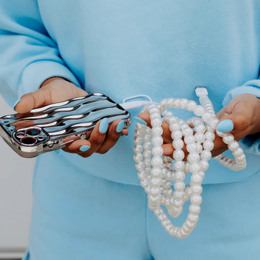 Person holding a phone with a reflective case and a string of pearls.