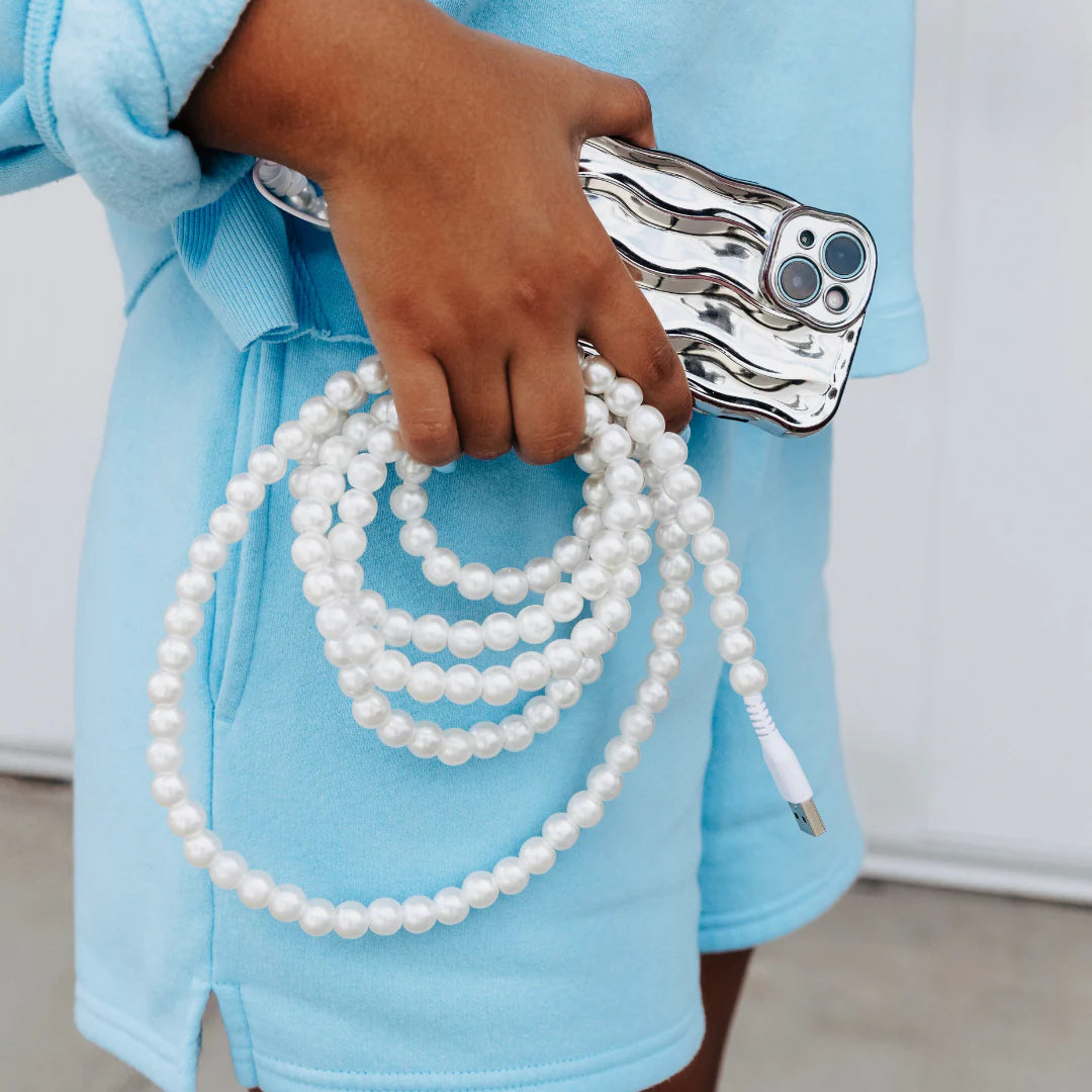 Person holding a bundle of white pearls with a silver clasp against a light blue background