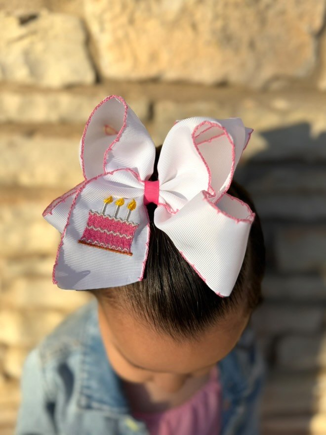 Large white hair bow with pink cake design on a blurred stone wall background