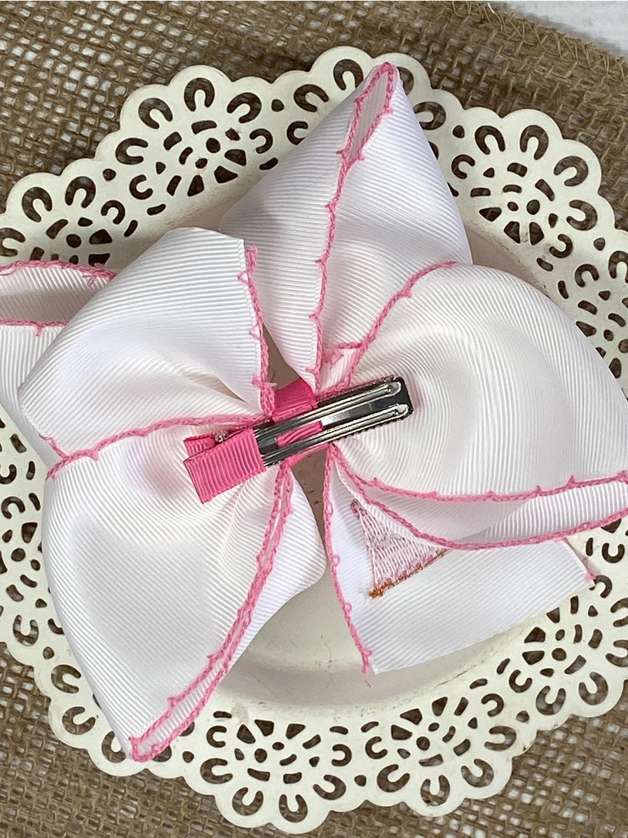 White hair bow with pink stitching on a decorative white plate