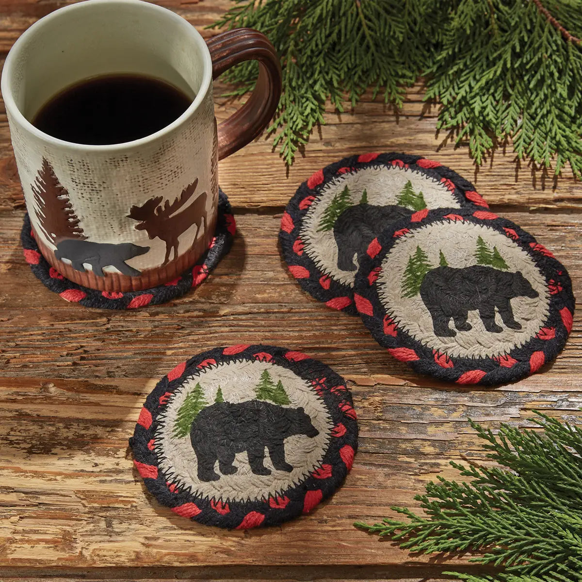 Mug with bear-themed coasters on a wooden surface with greenery