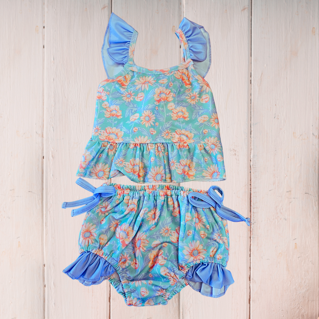 Floral baby romper with ruffled details on a wooden surface