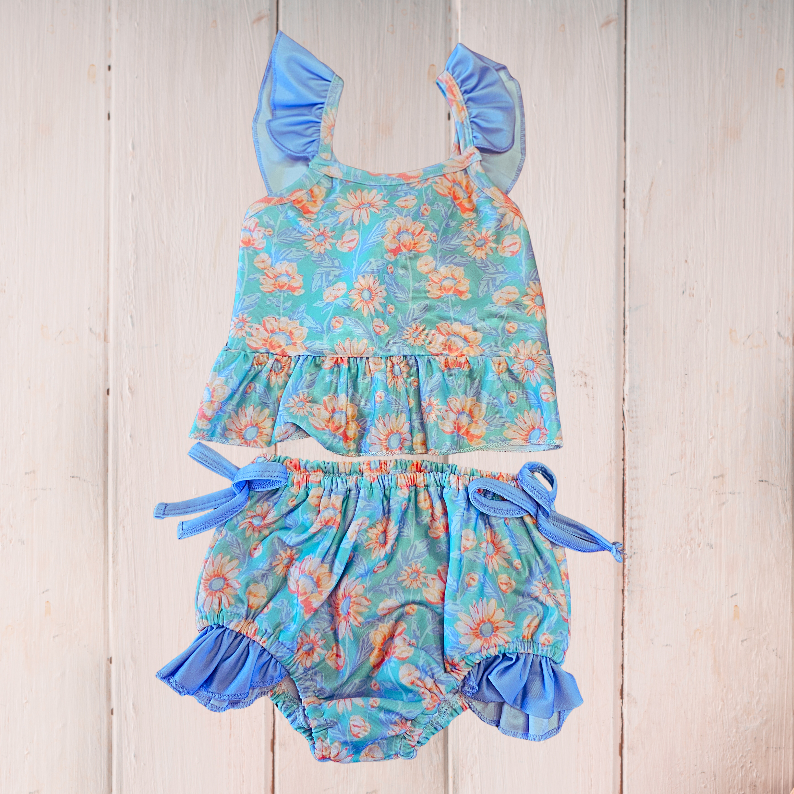 Floral baby romper with ruffled details on a wooden surface
