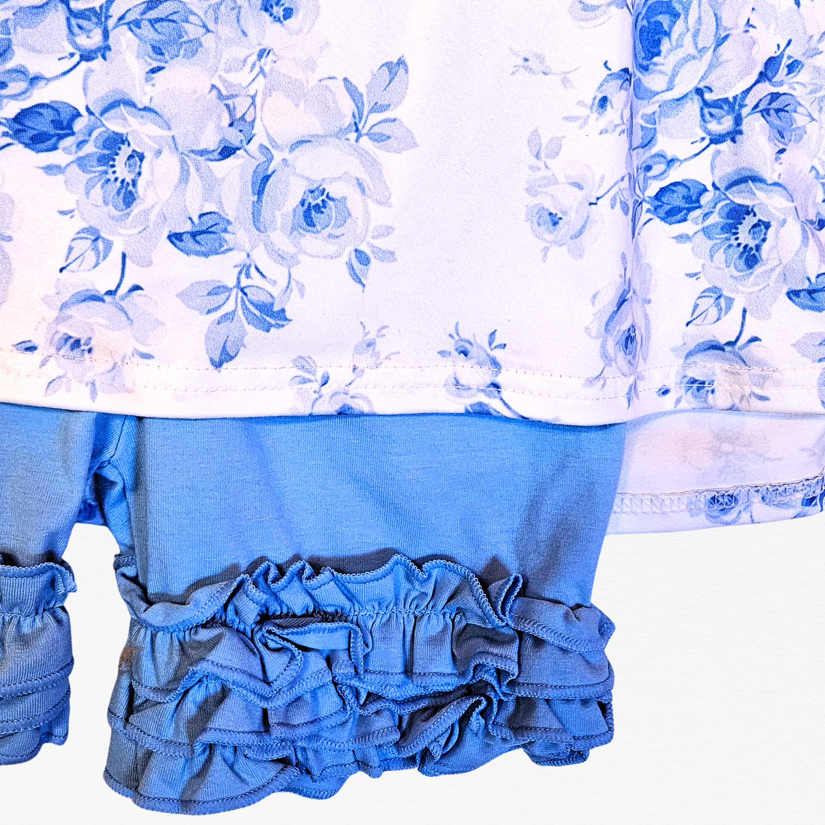 Children's outfit with floral top and blue ruffled shorts on a white background