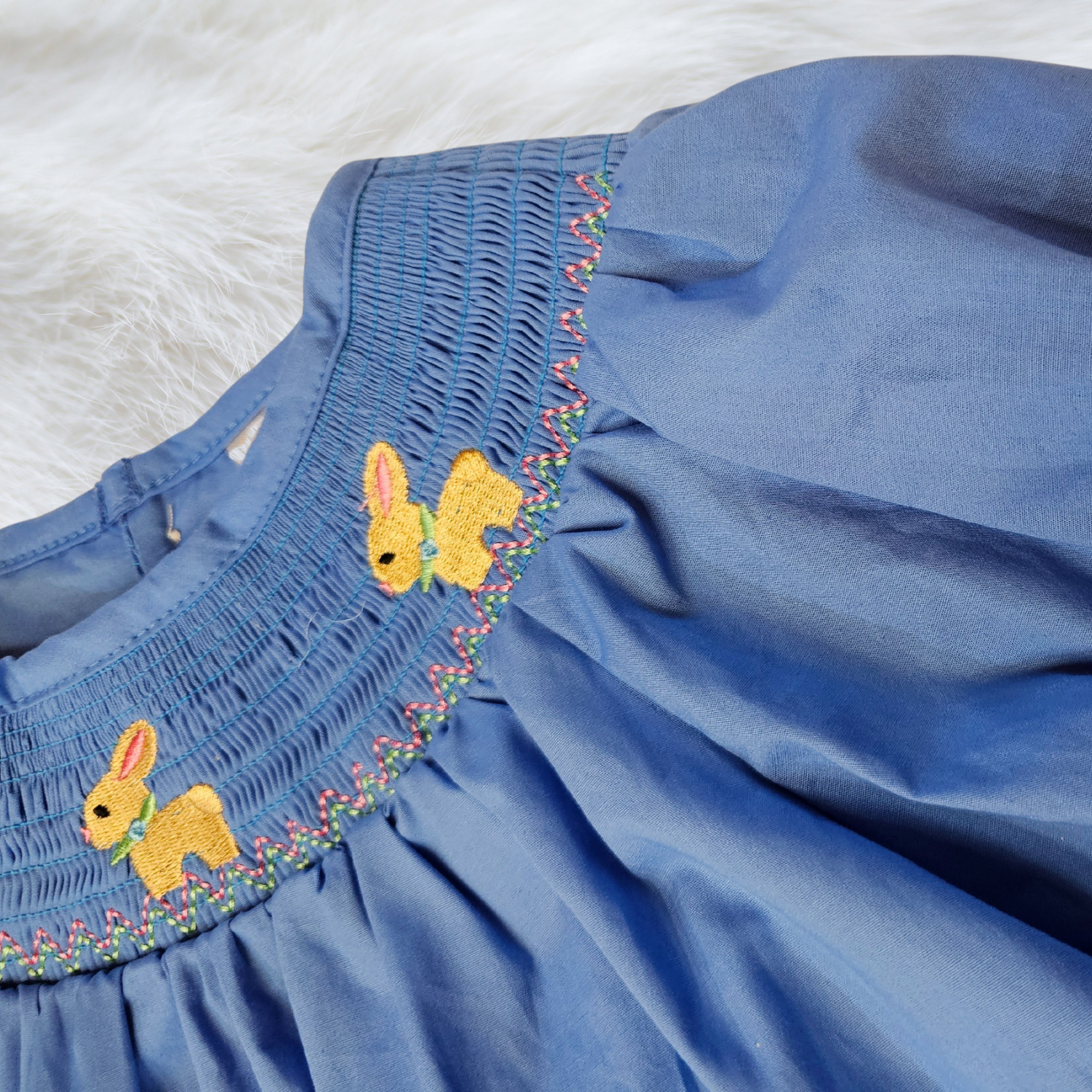 Blue dress with embroidered yellow bunnies on a white background