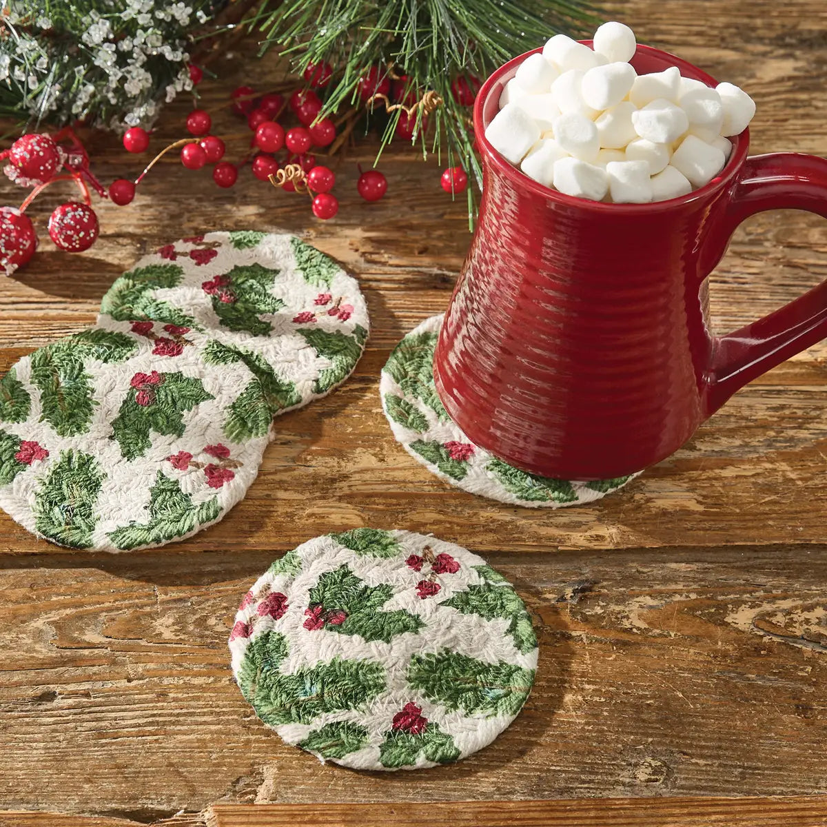 Red mug with marshmallows on a wooden table with Christmas-themed coasters.
