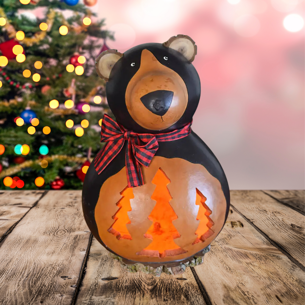 Decorative bear-shaped gourd lantern with a bow, Christmas tree design, and blurred Christmas tree in the background.