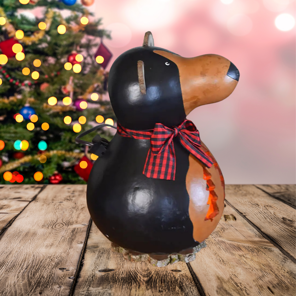 Decorative right side profile gourd shaped like a bear with a plaid ribbon on a wooden surface with a blurred Christmas tree in the background.