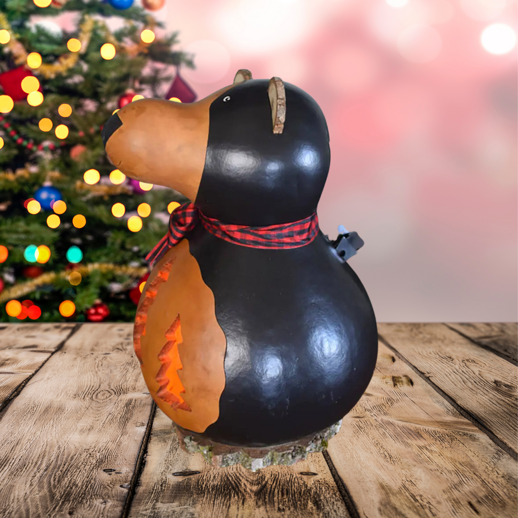Decorative left side profile gourd shaped like a bear with a plaid ribbon on a wooden surface with a blurred Christmas tree in the background.