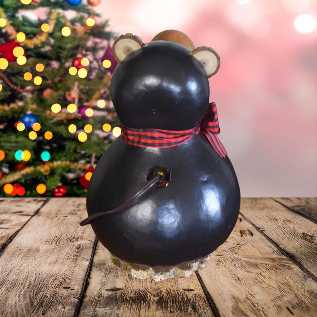 Decorative back of the bear-shaped gourd lantern with a bow, with plug showing, Christmas tree design, and blurred Christmas tree in the background.