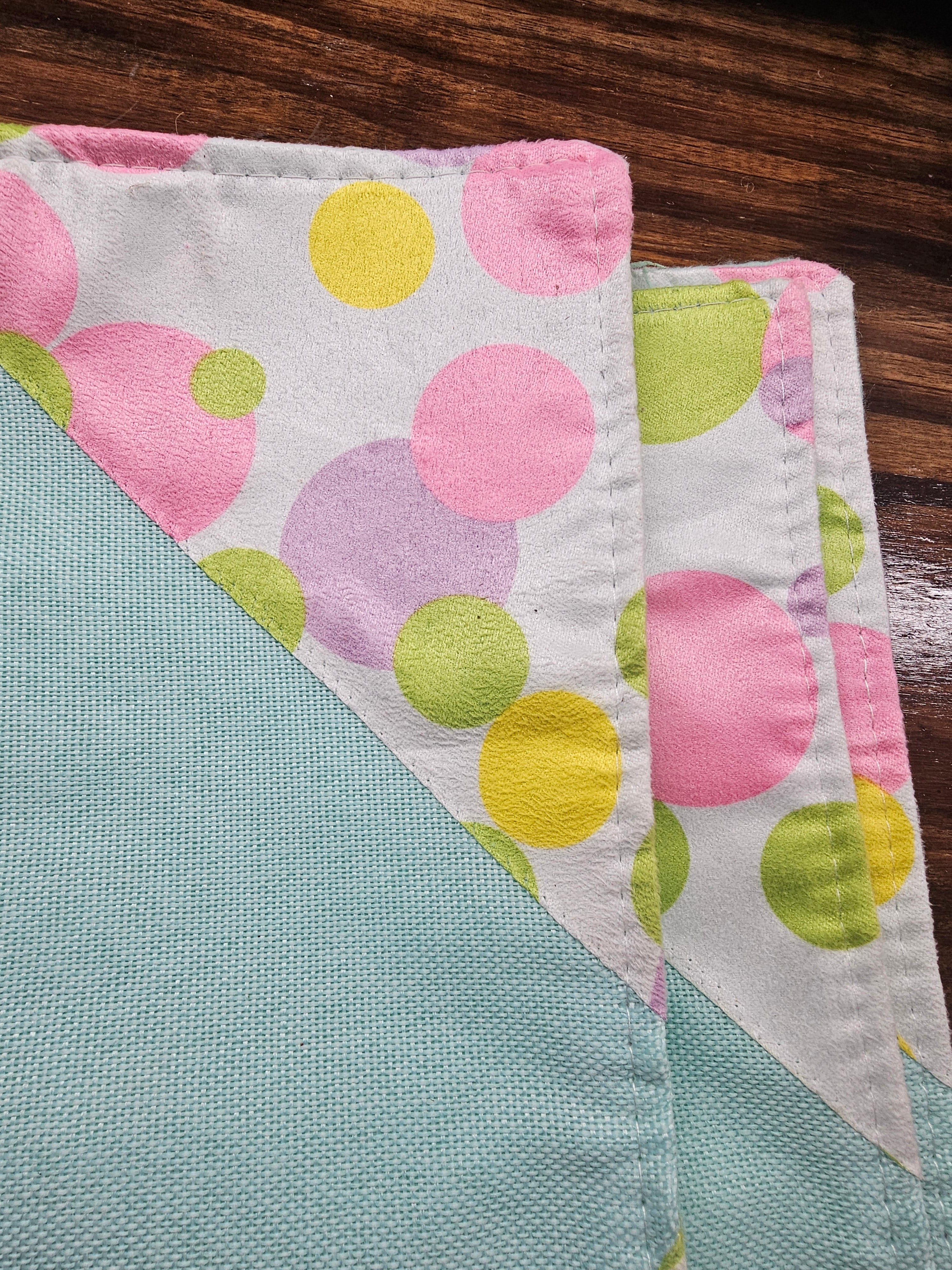 Two fabric placemats with colorful polka dots on a wooden surface