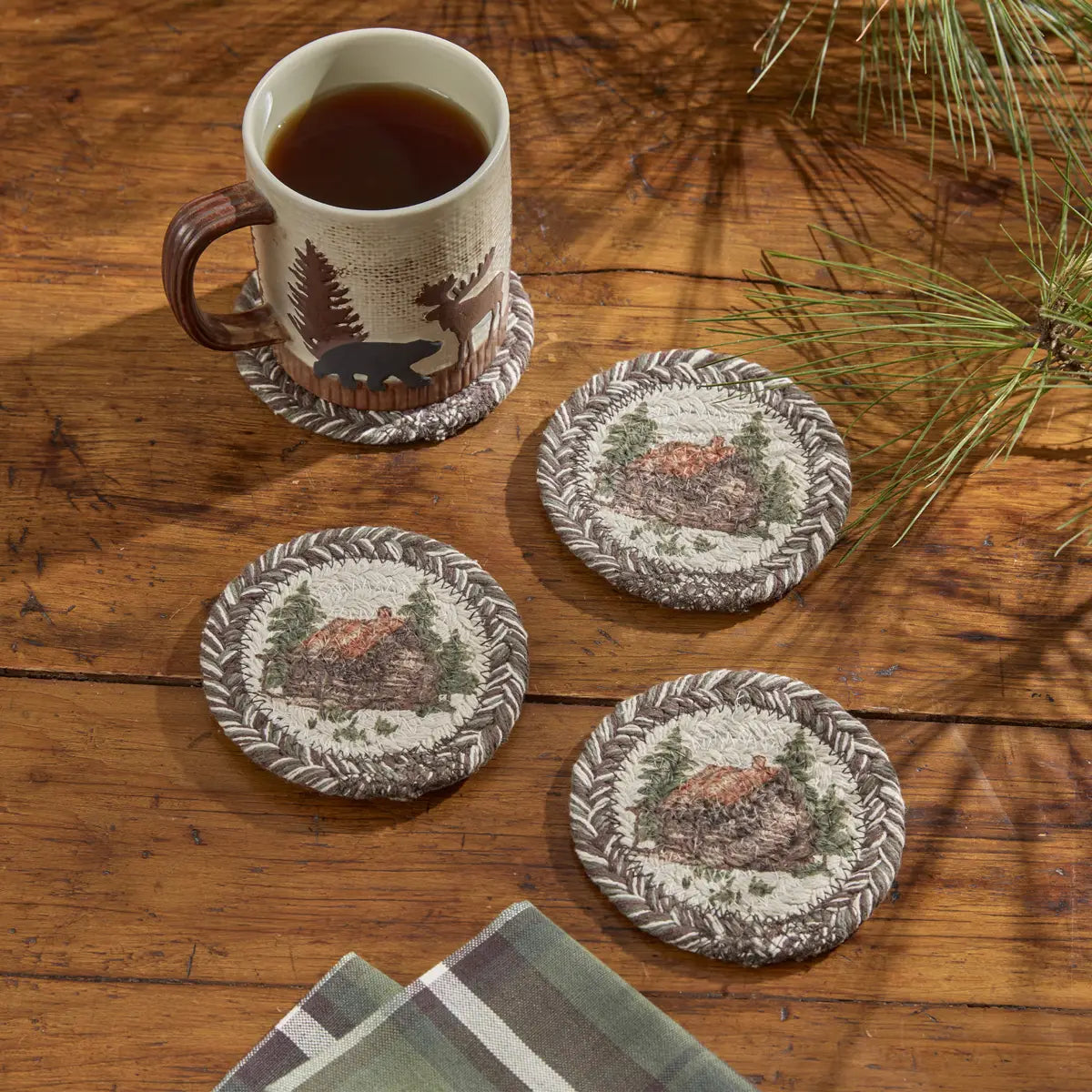 Set of four coasters with nature-themed designs on a wooden surface with a mug of tea.