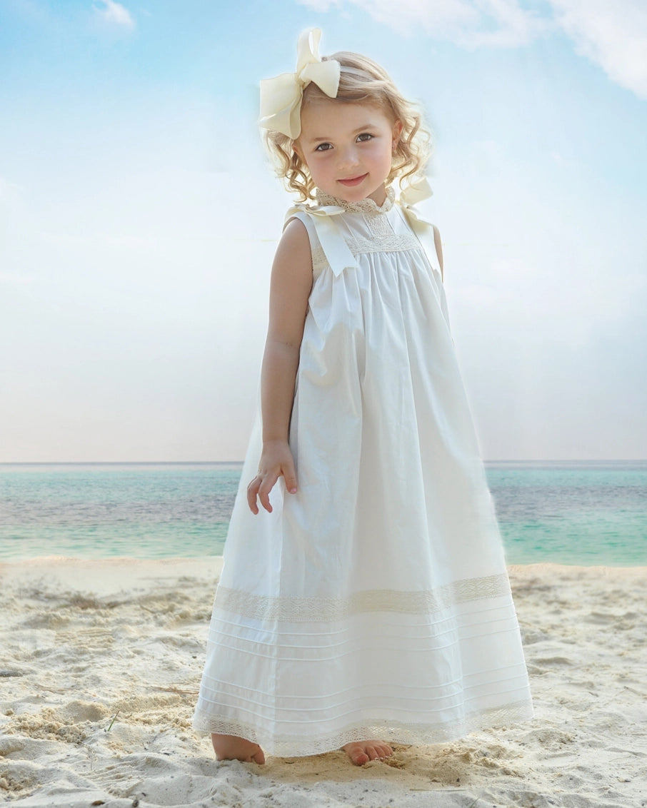 Young girl in a white dress standing on a beach with ocean and sky in the background