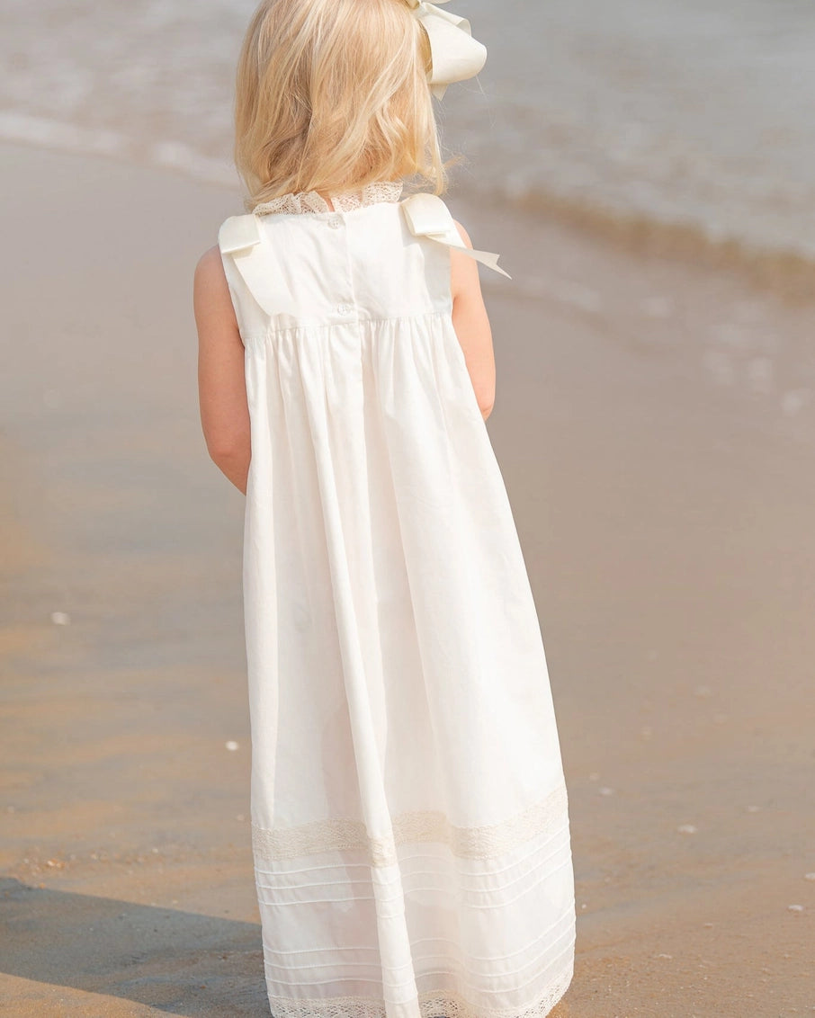 Young girl in a white dress standing on a sandy beach.