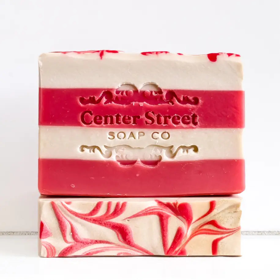 Two striped red and white soap bars with 'Center Street Soap Co' branding on a light wooden surface.