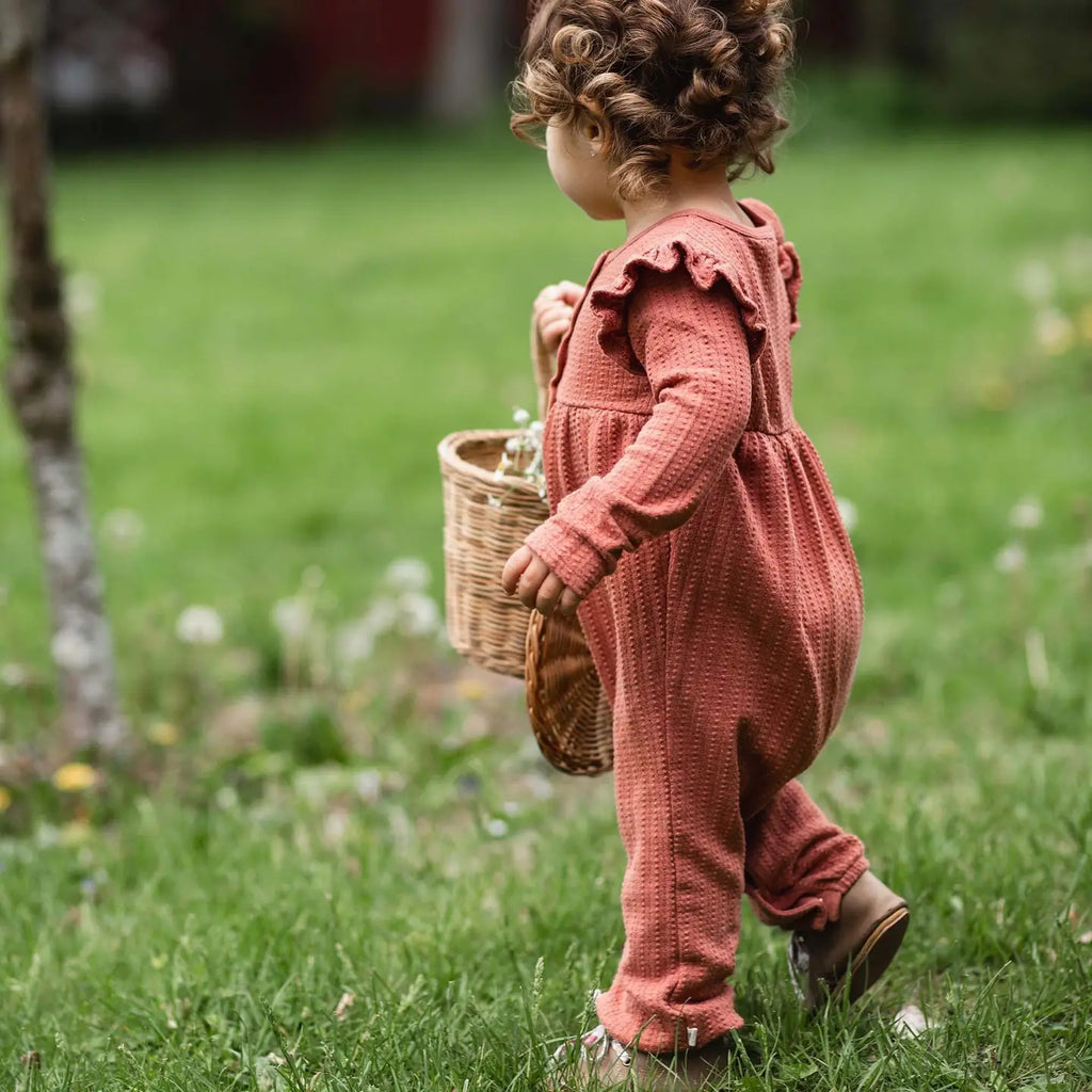 Child in a pink knitted outfit holding a wicker basket in a grassy outdoor setting