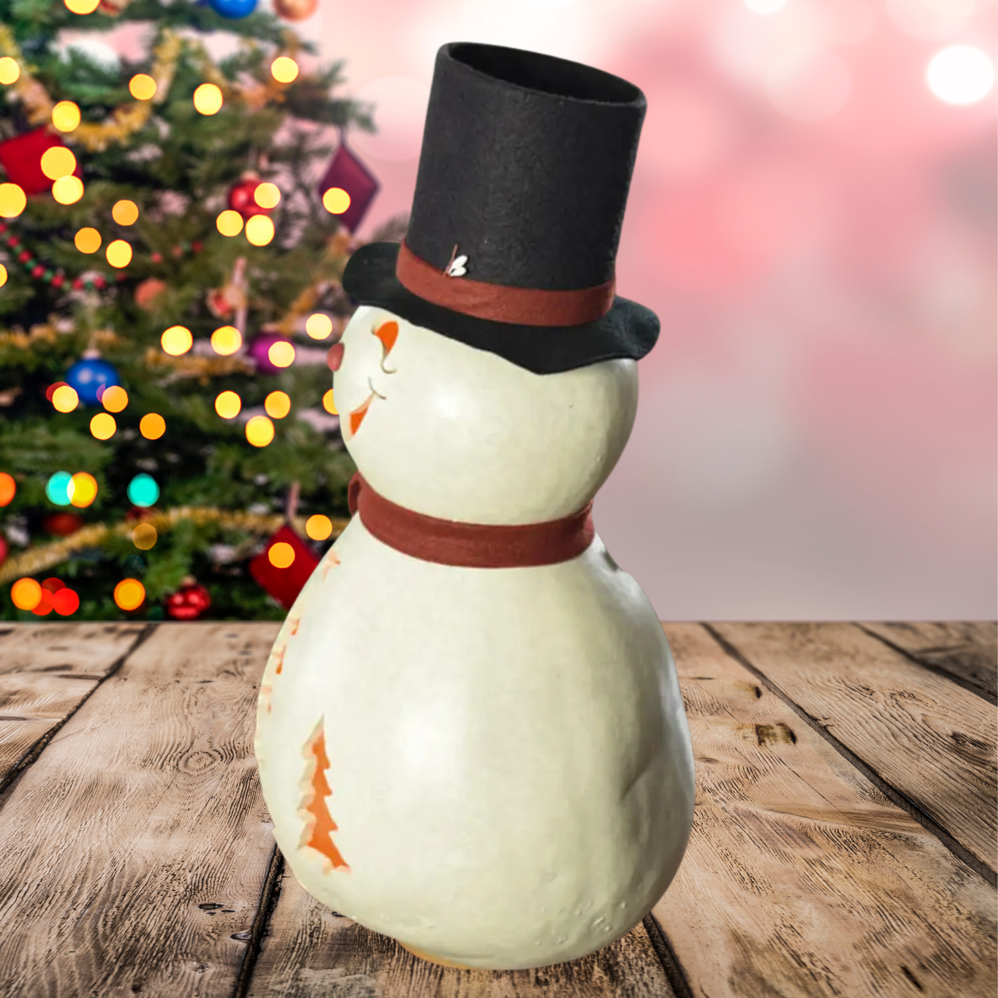 Snowman figurine left side profile with a top hat on a wooden surface with a blurred Christmas tree in the background.