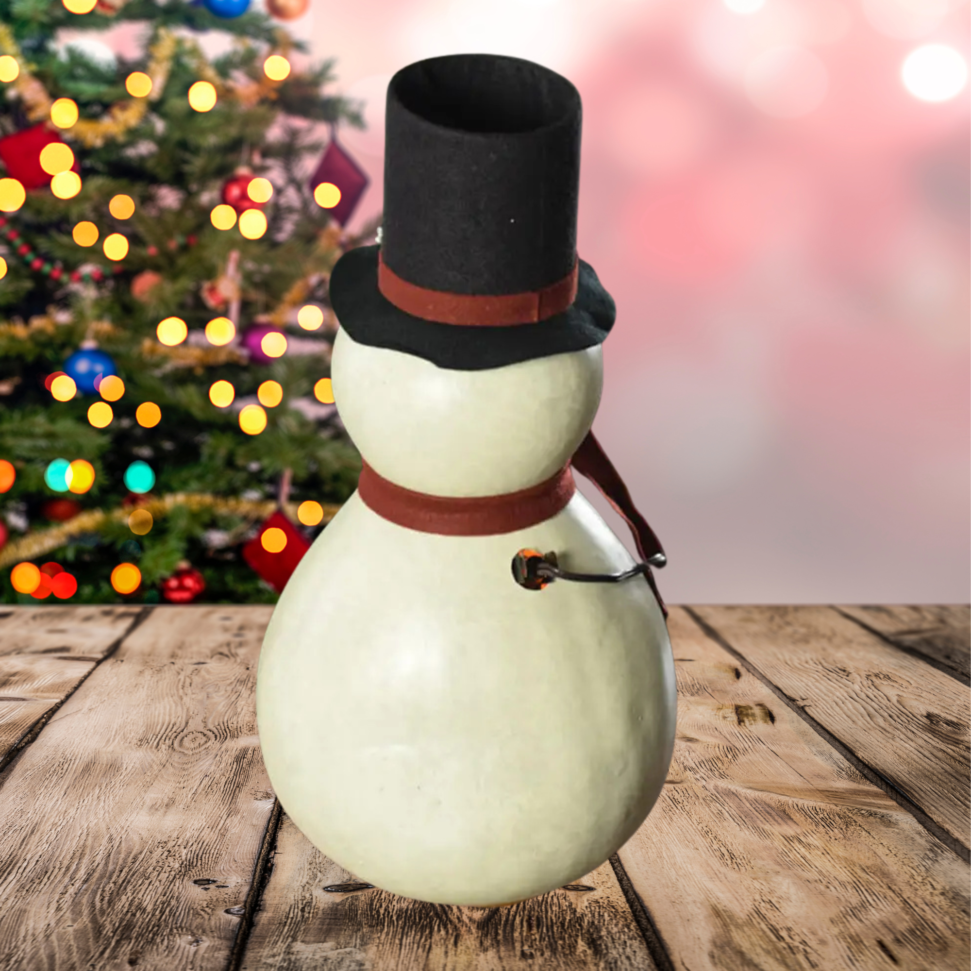 Snowman decoration with a black top hat with a plug showing on a wooden surface with a blurred Christmas tree in the background.
