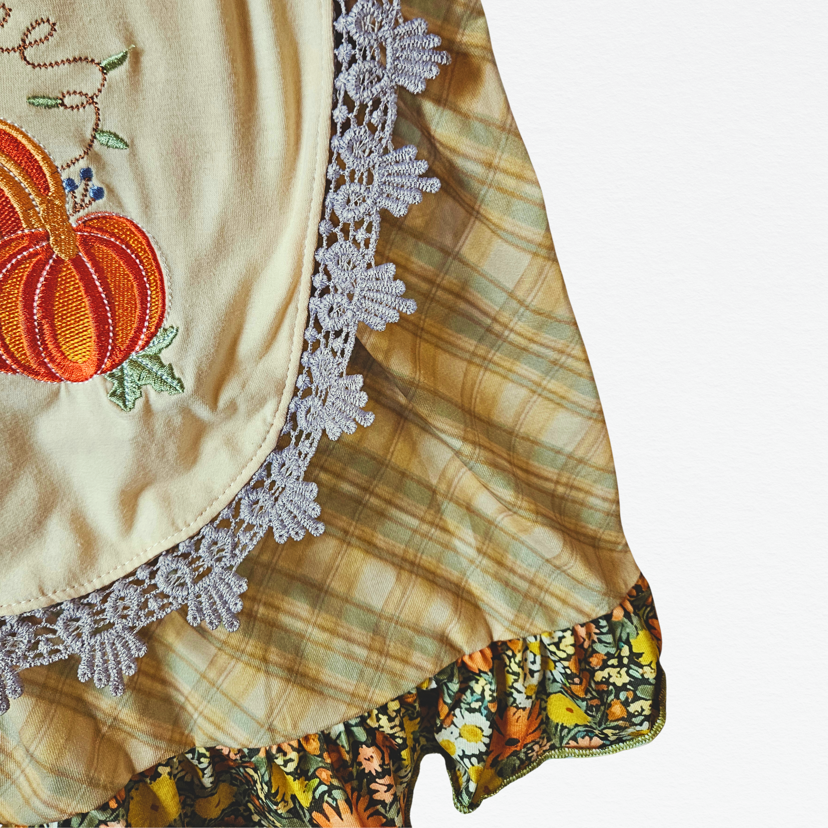 Embroidered pumpkin design on a fabric with lace trim and plaid pattern.