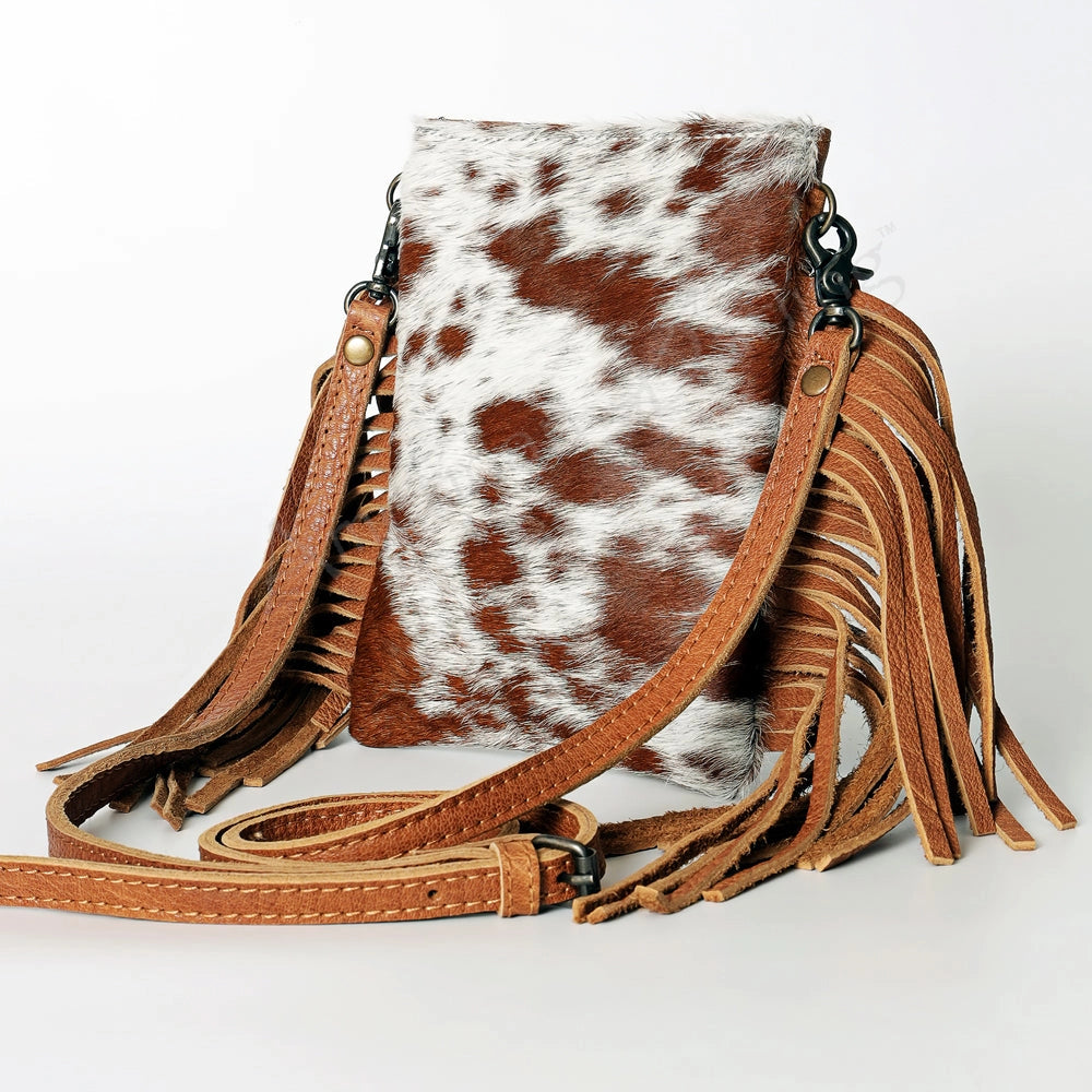 Brown and white cowhide leather crossbody bag with fringes on a light gray background