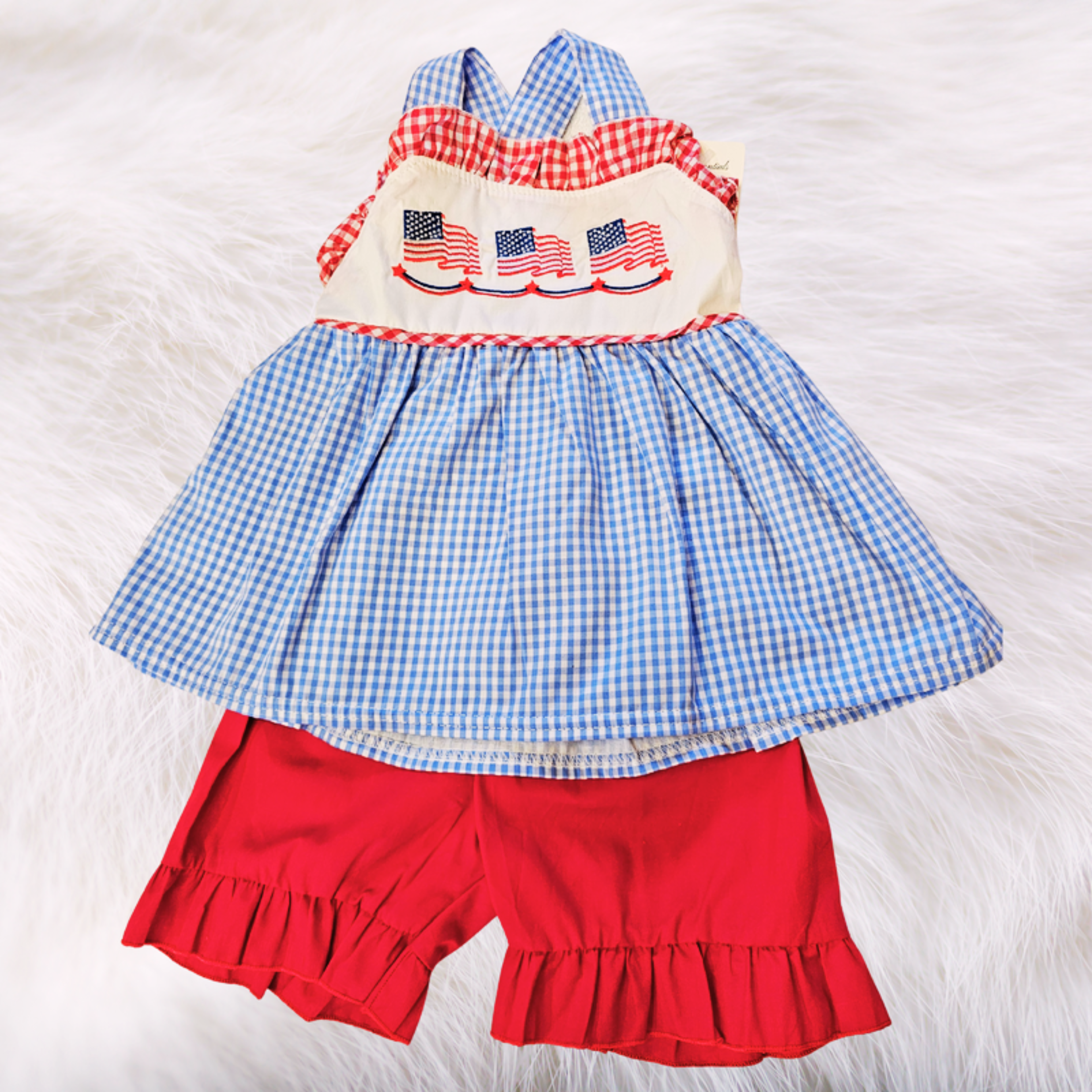 Children's outfit with blue checkered top, red shorts, and American flag design on a white background