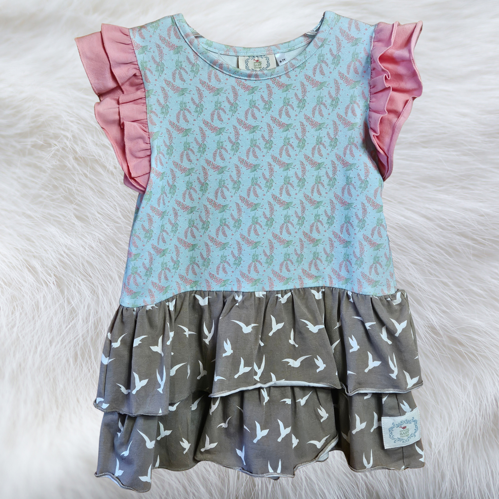 Two-tiered dress with pink ruffled sleeves and patterned layers on a white fur background